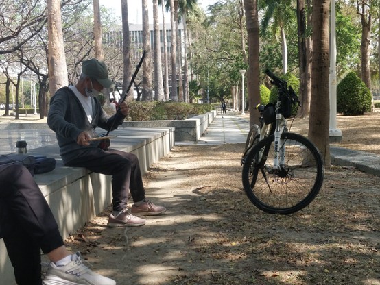 在公園彈著二胡的爺爺，還有一輛停著的腳踏車