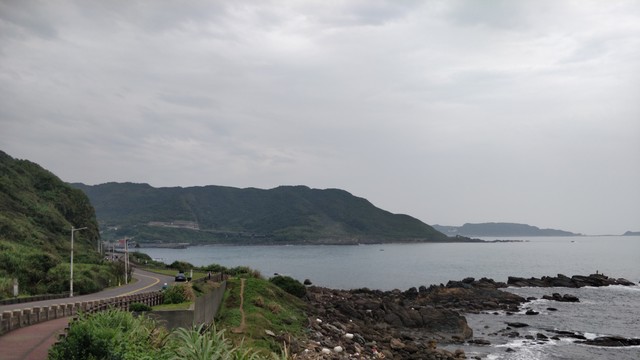 從野柳西邊拍的照片。陰天，左邊有公路跟自行車道，前面有岩岸，後面有山